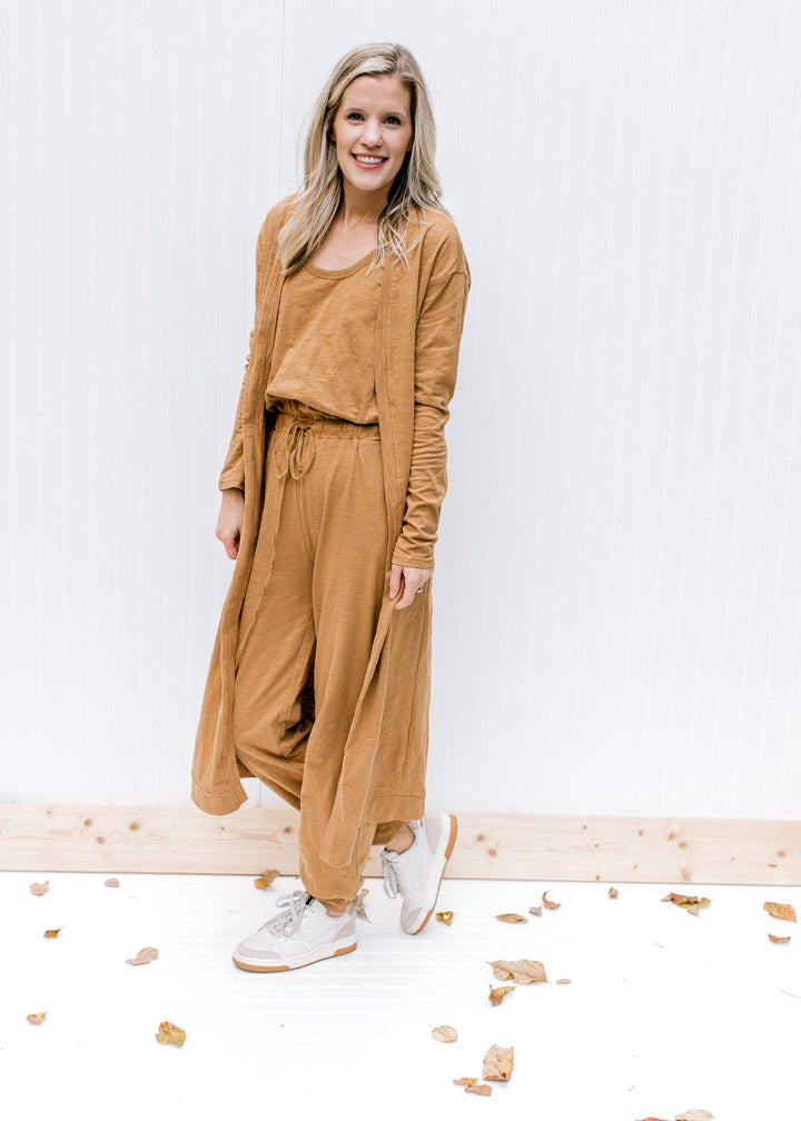 Model wearing sneakers and a mocha jumpsuit with tie at the waist and a matching cardigan. 