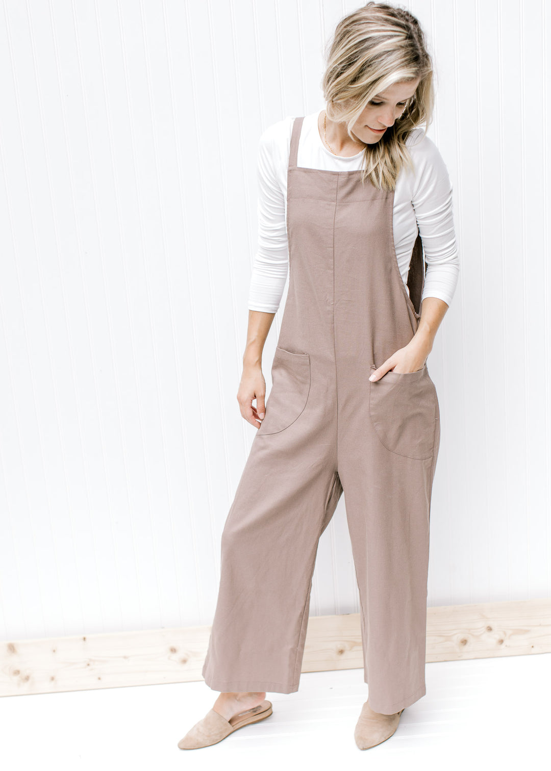 Model wearing mules and a white top with a mocha jumpsuit that has wide legs and adjustable straps.