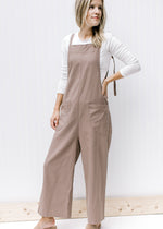 Model wearing a mocha jumpsuit with patch pockets, square neckline, wide legs and adjustable straps.