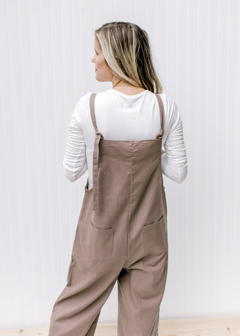 Back view of Model wearing a mocha jumpsuit with a square neckline, wide legs and adjustable straps.