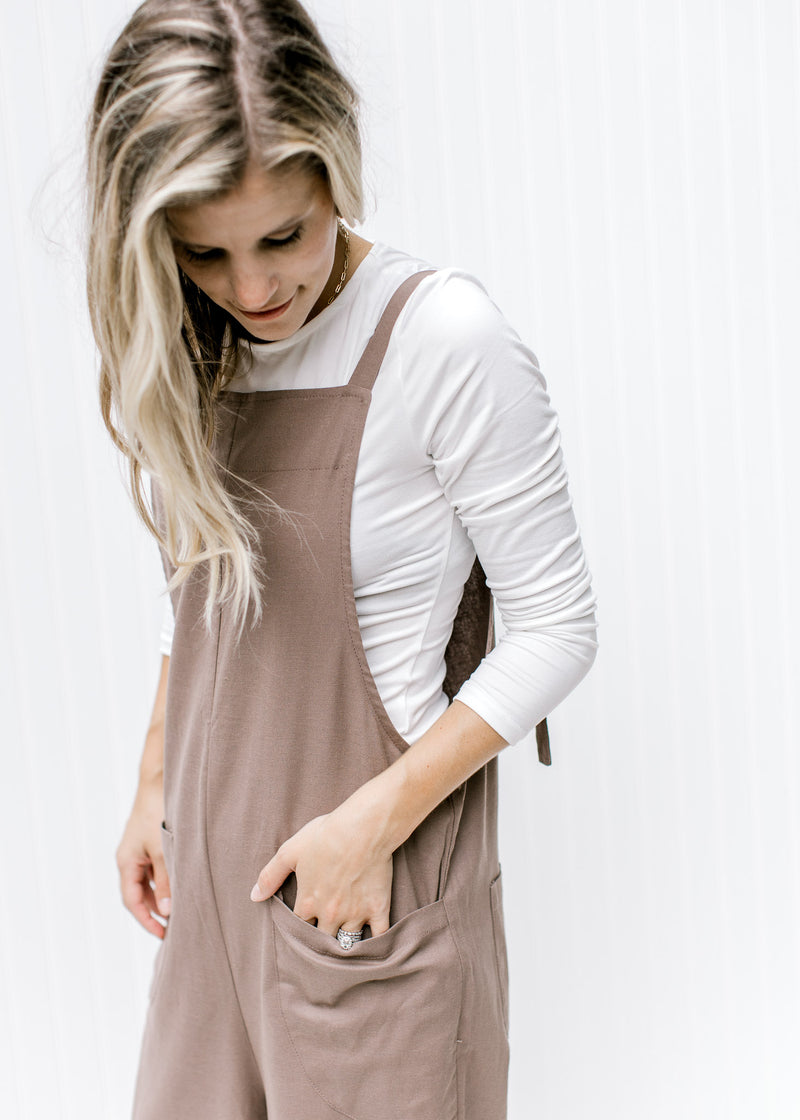 Model wearing a mocha jumpsuit with patch pockets, square neckline and adjustable straps. 
