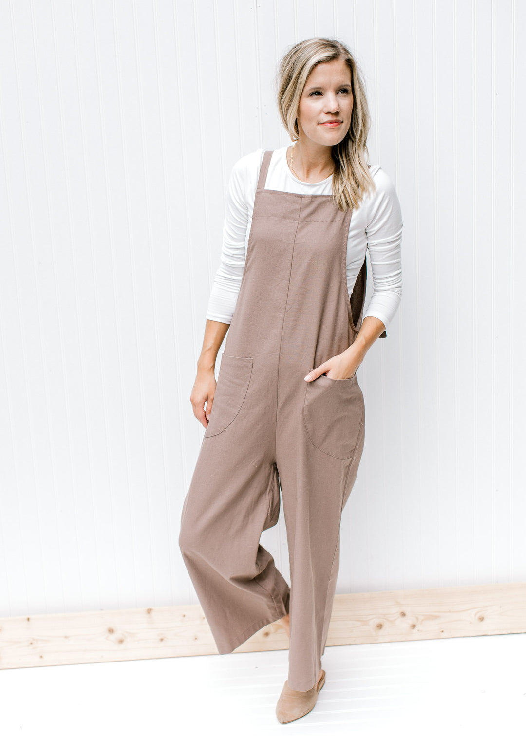 Model wearing a white top with a mocha jumpsuit that has wide legs and adjustable straps.