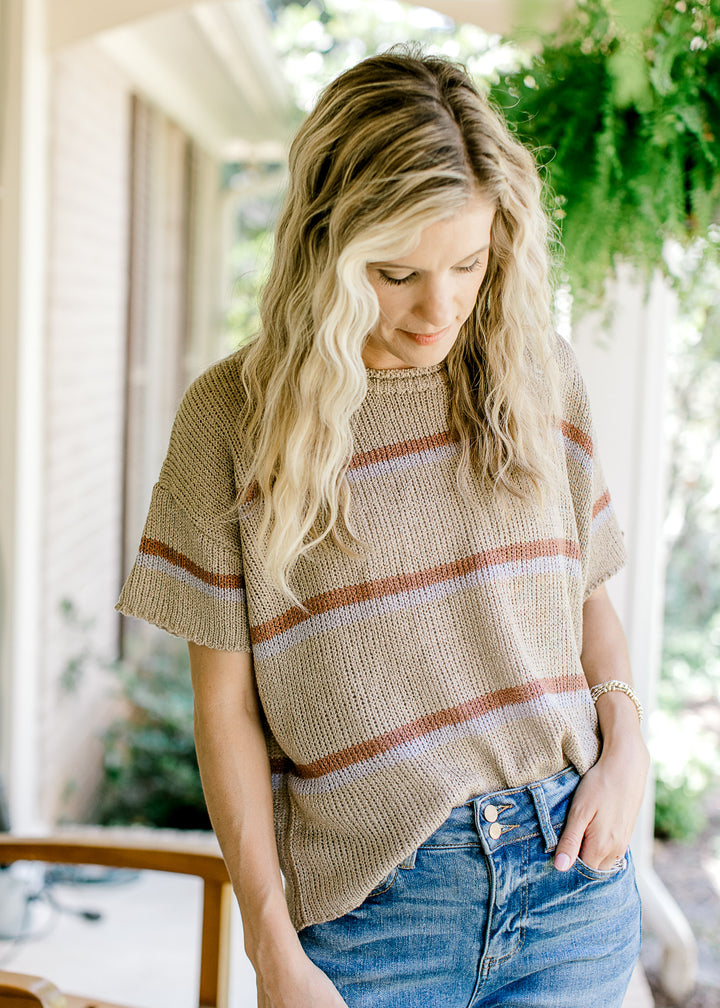Model wearing a taupe top with brown and gray stripes, comprised of a light weave and short sleeves.