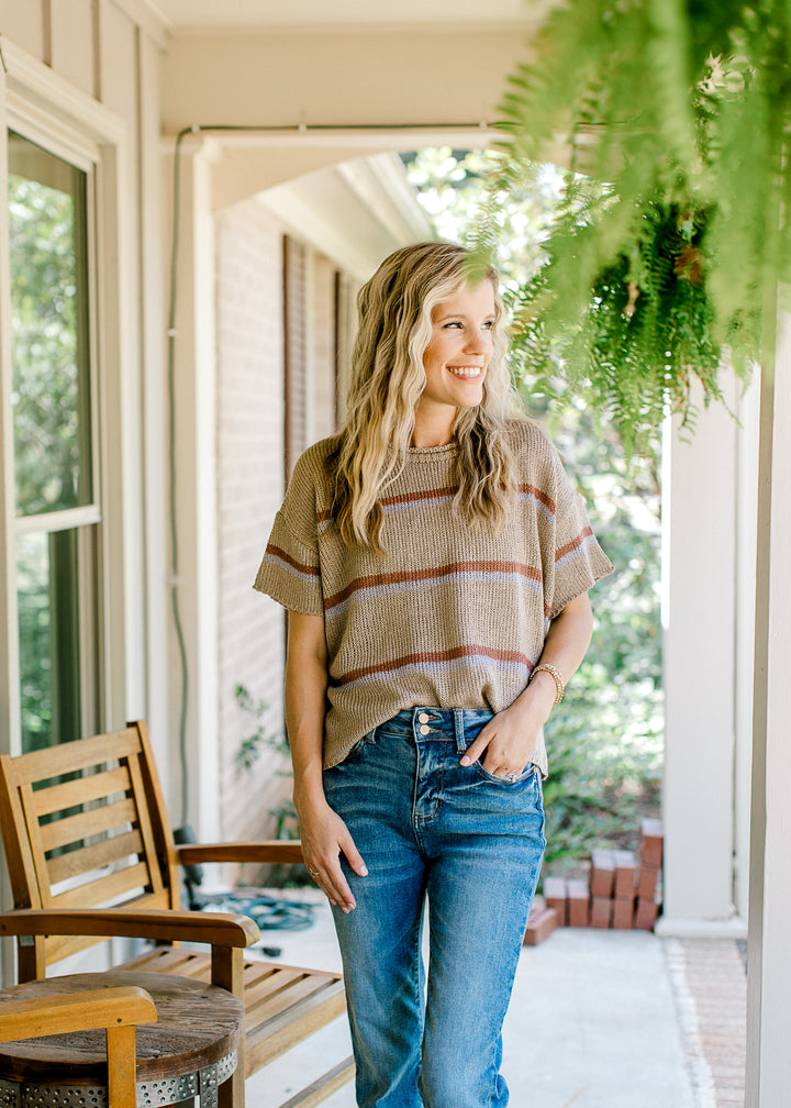 Model wearing jeans and a taupe ribbed top with brown and gray stripes. 