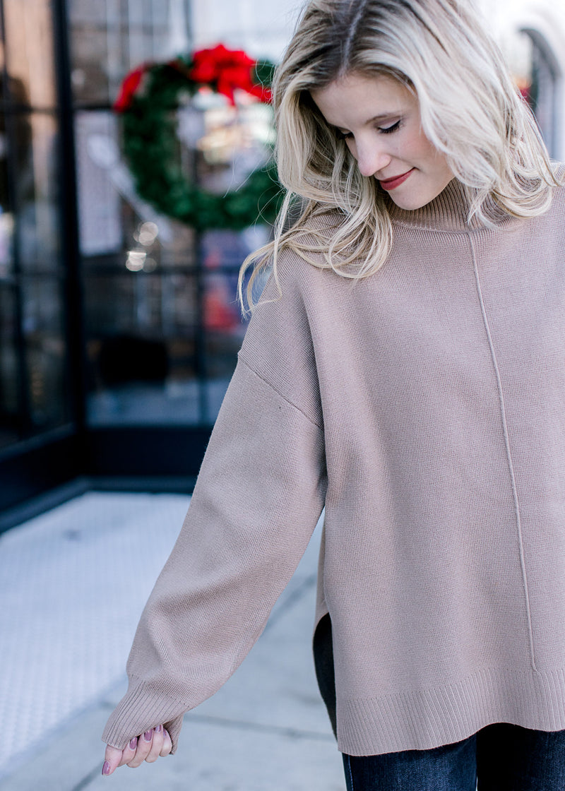 Model wearing a mocha sweater with a mock neck, long sleeves and extended shoulder. 