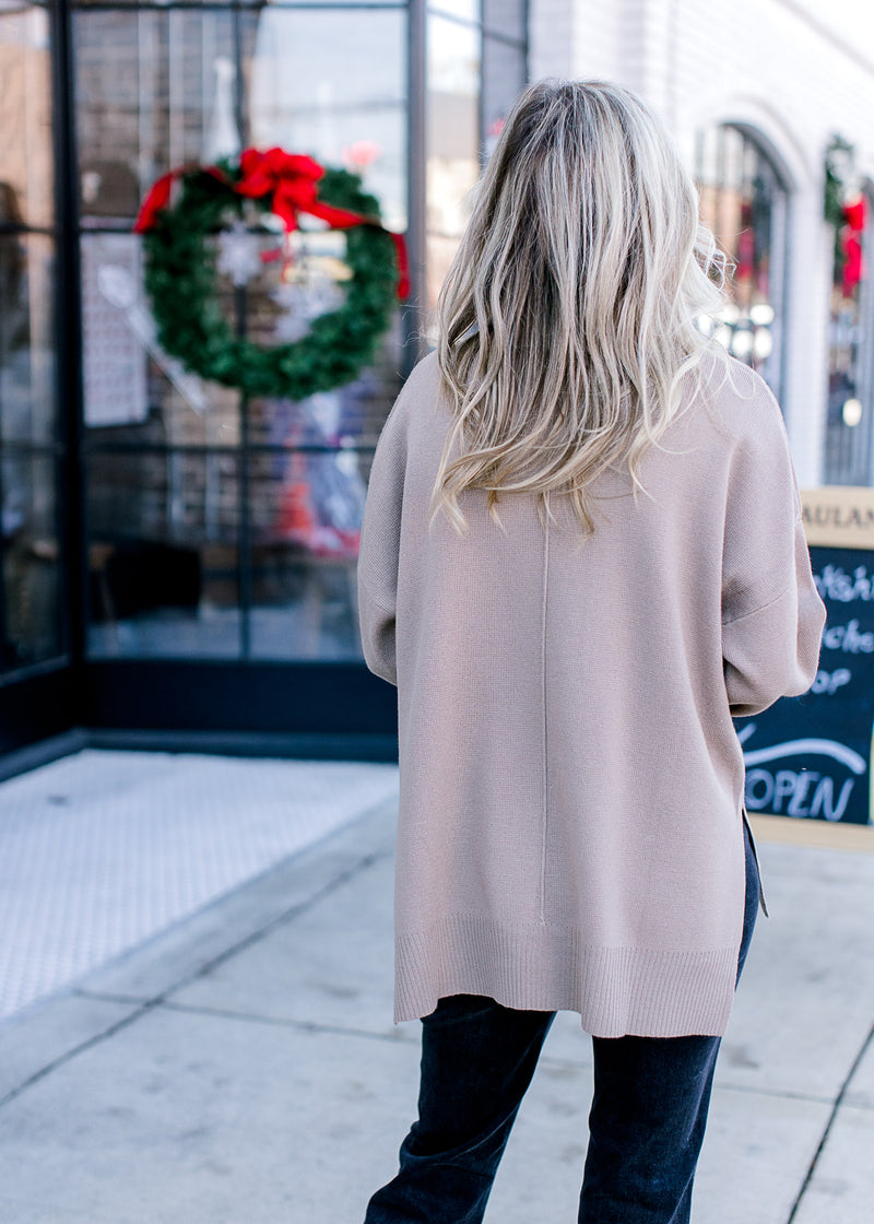 Back view of Model wearing a mocha sweater with a mock neck, long sleeves and split sides.