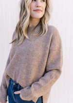 Model wearing a taupe sweater with ribbed detailing, a round neck and long sleeves.