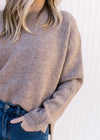 Close up of ribbed detailing and round neck on a model wearing a taupe, long sleeve sweater. 