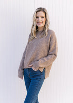 Model wearing a taupe sweater with split sides, a round neck and long sleeves.