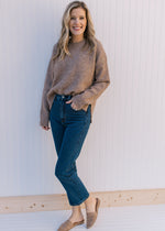 Model wearing jeans with a taupe sweater with a round neck and long sleeves.