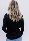Back view of Model wearing a fitted black ribbed top with a mock neckline and long sleeves. 