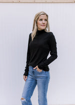 Model wearing jeans with a fitted black ribbed top with a mock neckline and long sleeves. 