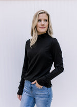 Model wearing a fitted black ribbed top with a mock neckline and long sleeves. 