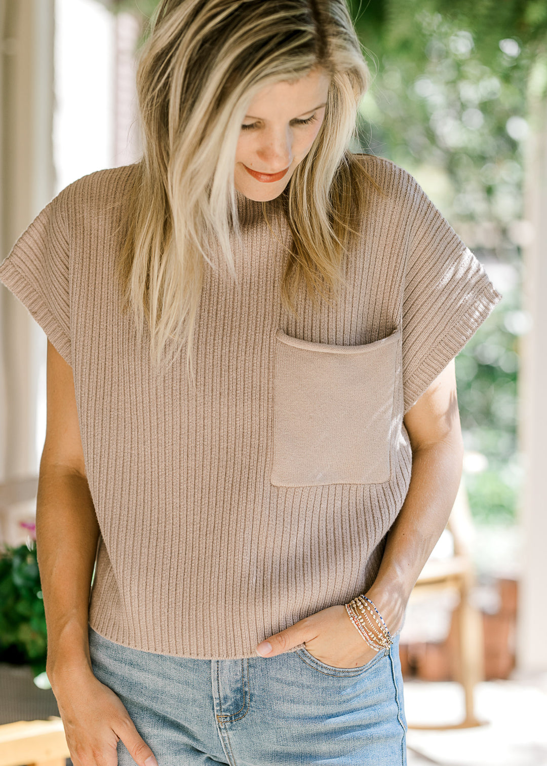 Model wearing a tan ribbed sweater with extended shoulder short sleeves and a patch pocket. 