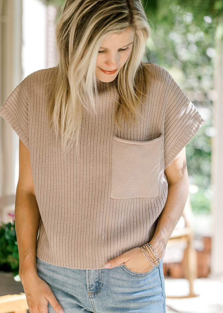 Model wearing a tan ribbed sweater with extended shoulder short sleeves and a patch pocket. 