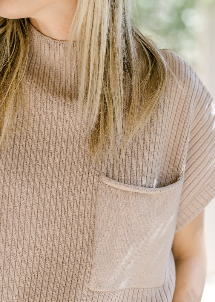 Close up of mock neck and patch pocket on a tan ribbed sweater with short sleeves. 