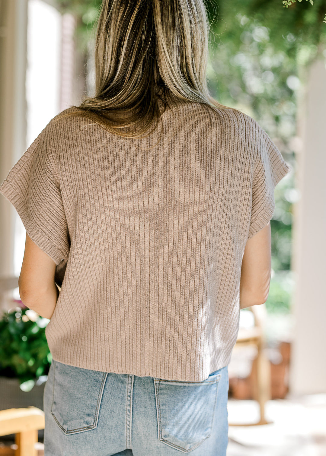 Back view of Model wearing a tan ribbed sweater with extended shoulder short sleeves. 