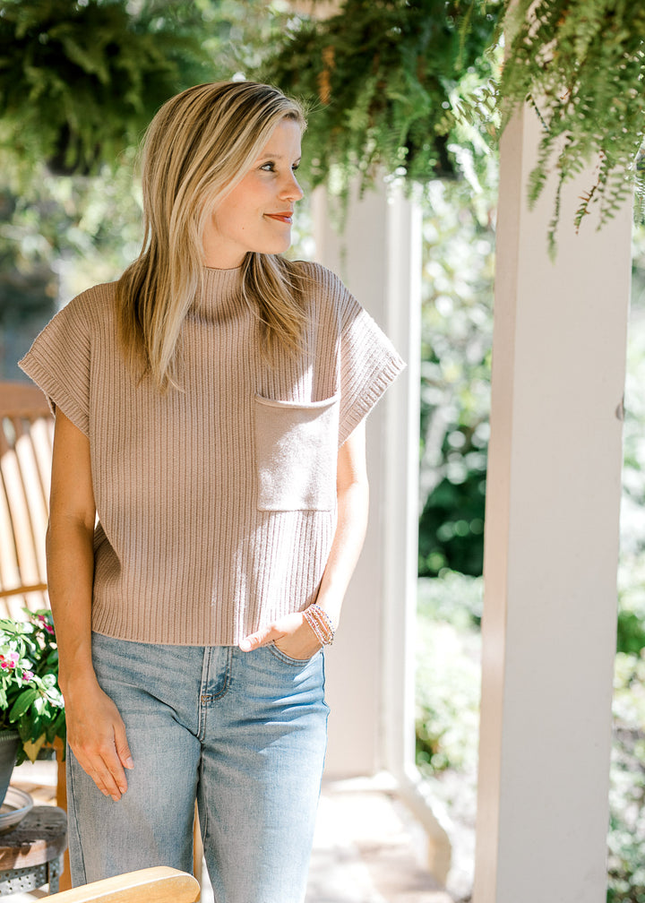 Model wearing jeans and a tan ribbed sweater with short sleeves and a patch pocket. 