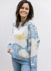 Model wearing a pale blue sweater with cream and yellow floral, long sleeves and a round neck.