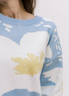 Close up of cream and yellow floral on a pale blue sweater with long sleeves and a round neck. 