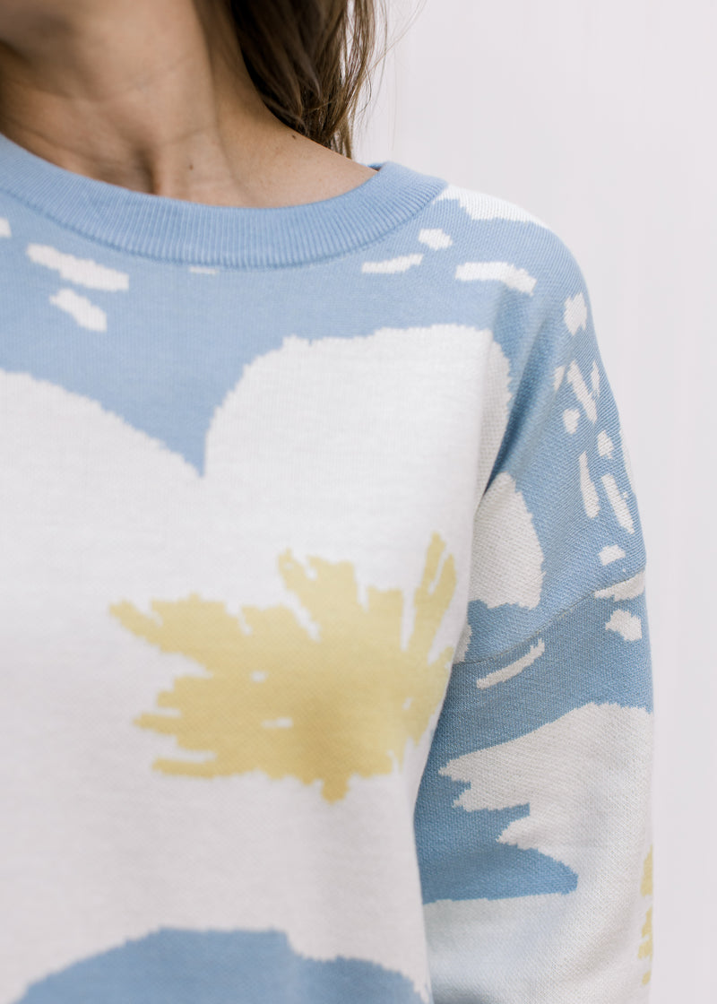 Close up of cream and yellow floral on a pale blue sweater with long sleeves and a round neck. 