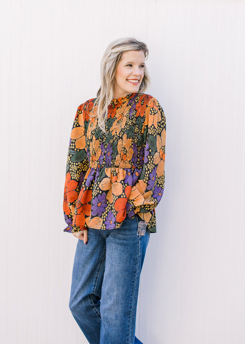 Model wearing a black top with bright floral, smocked bodice and poet long sleeves. 