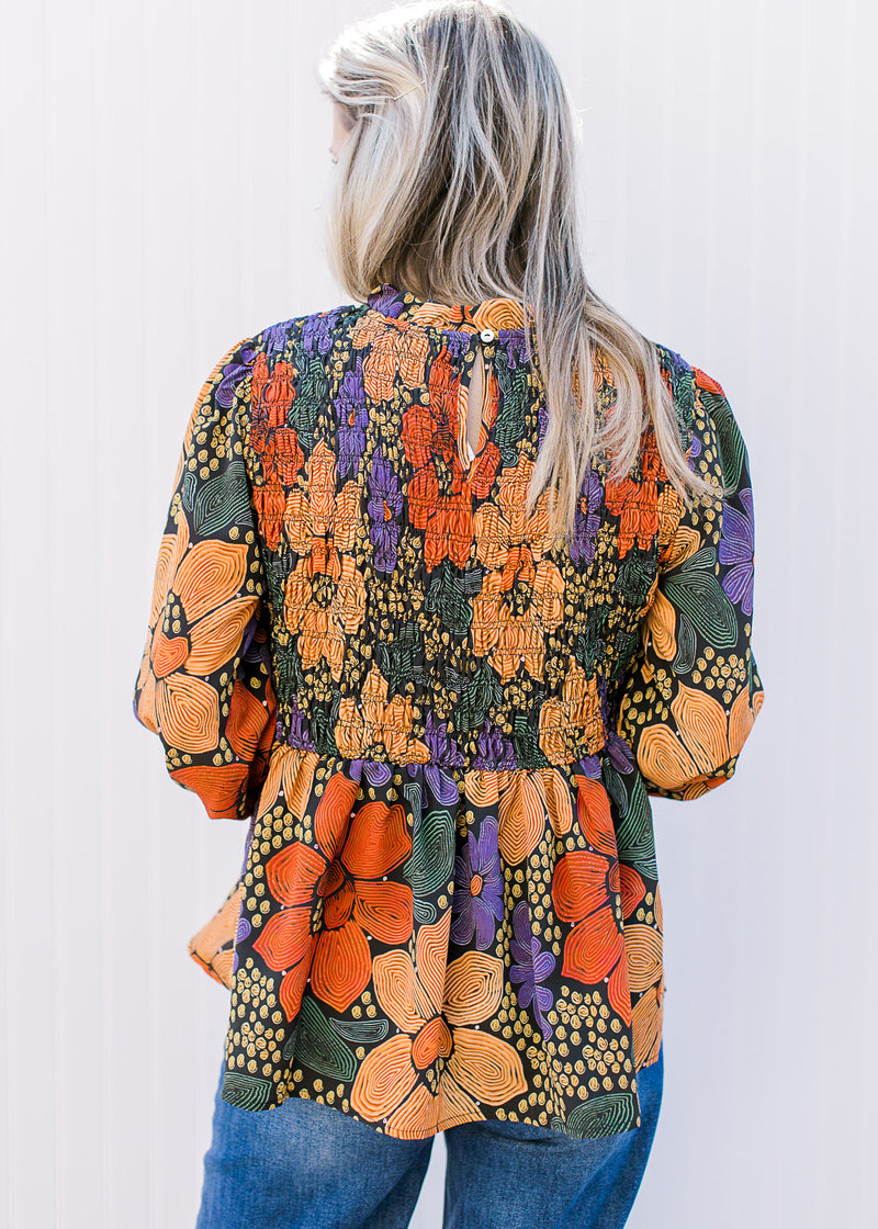 Back view of model wearing a black top with bright floral, smocked bodice and long sleeves. 