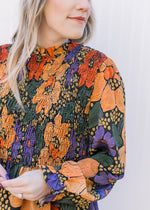 Close up of smocked bodice and poet long sleeves on a black top with bright floral pattern.