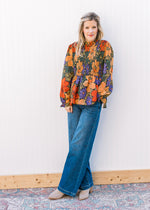 Model wearing jeans, booties and a black top with bright floral and poet long sleeves. 