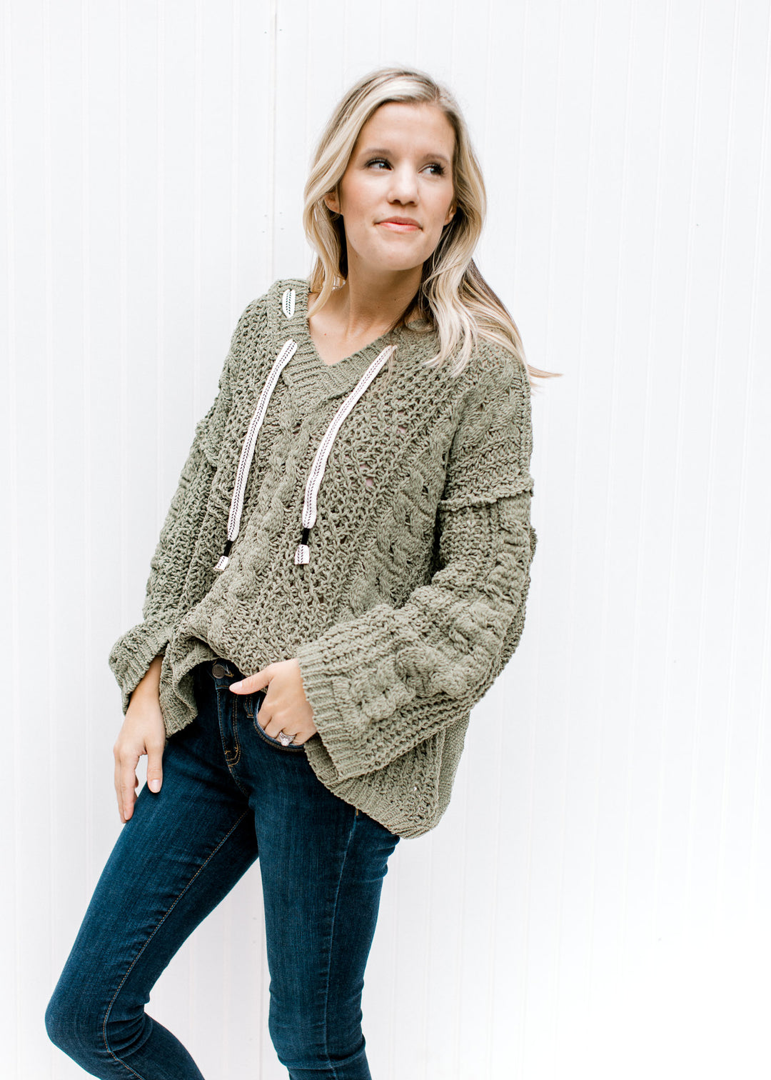 Model wearing jeans and a moss hoodie with long sleeves and a woven white string detail at the hood.