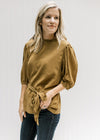 Model wearing a copper colored top with a ruffled neckline, bubble short sleeves and a tie at waist.