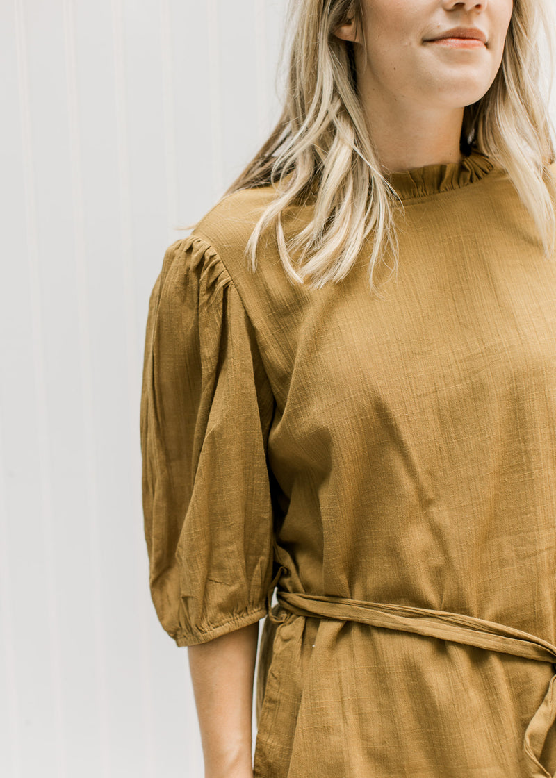 Close up of ruffled neck, bubble short sleeves and tie around the waist of a copper colored top. 