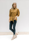 Model wearing jeans, booties and a copper colored short sleeve top with a ruffled neck and a tie. 