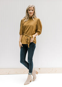 Model wearing jeans, booties and a copper colored short sleeve top with a ruffled neck and a tie. 