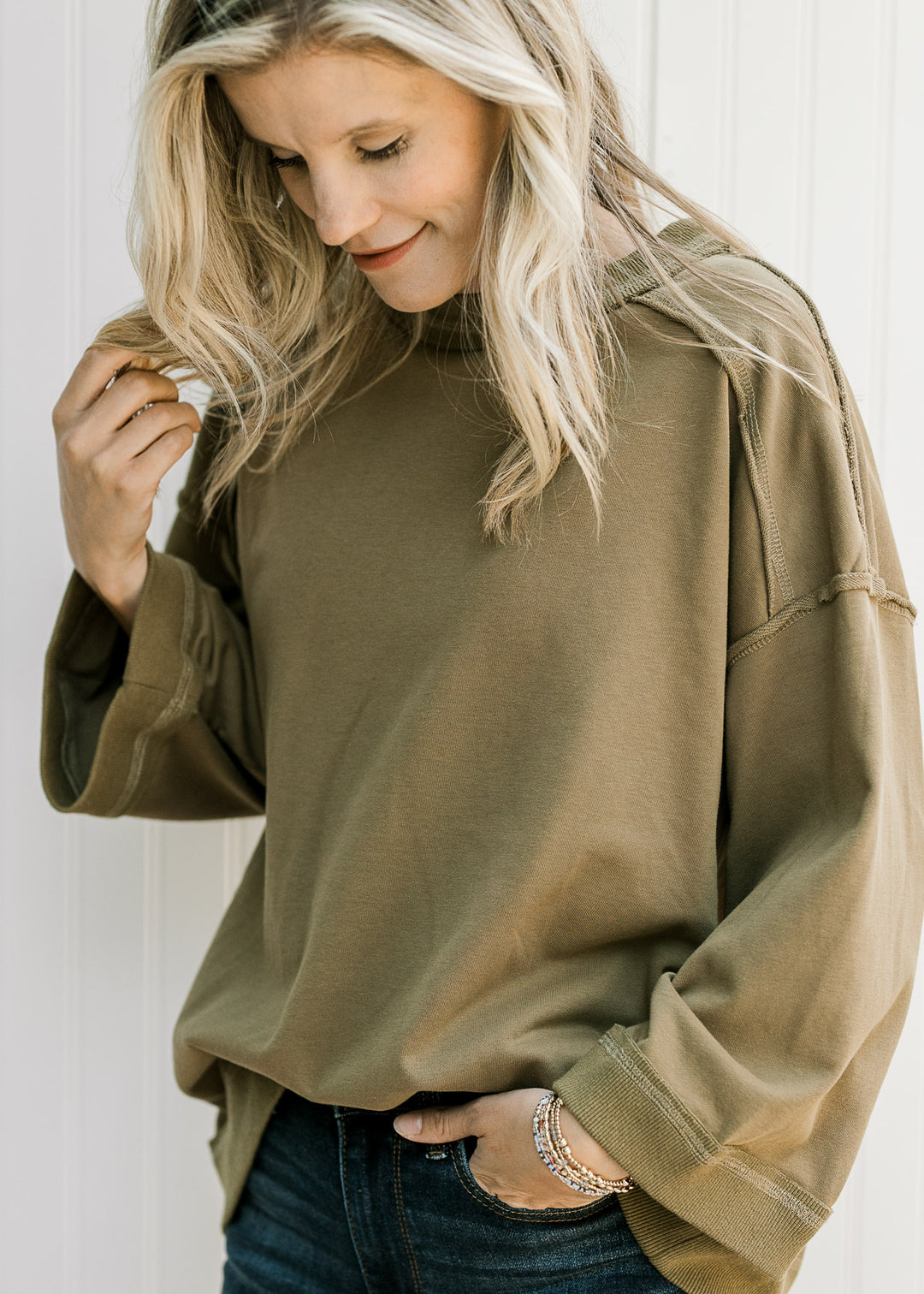 Model wearing an olive 3/4 sleeve top with ribbed detail, exposed hem and patch with seam on back.