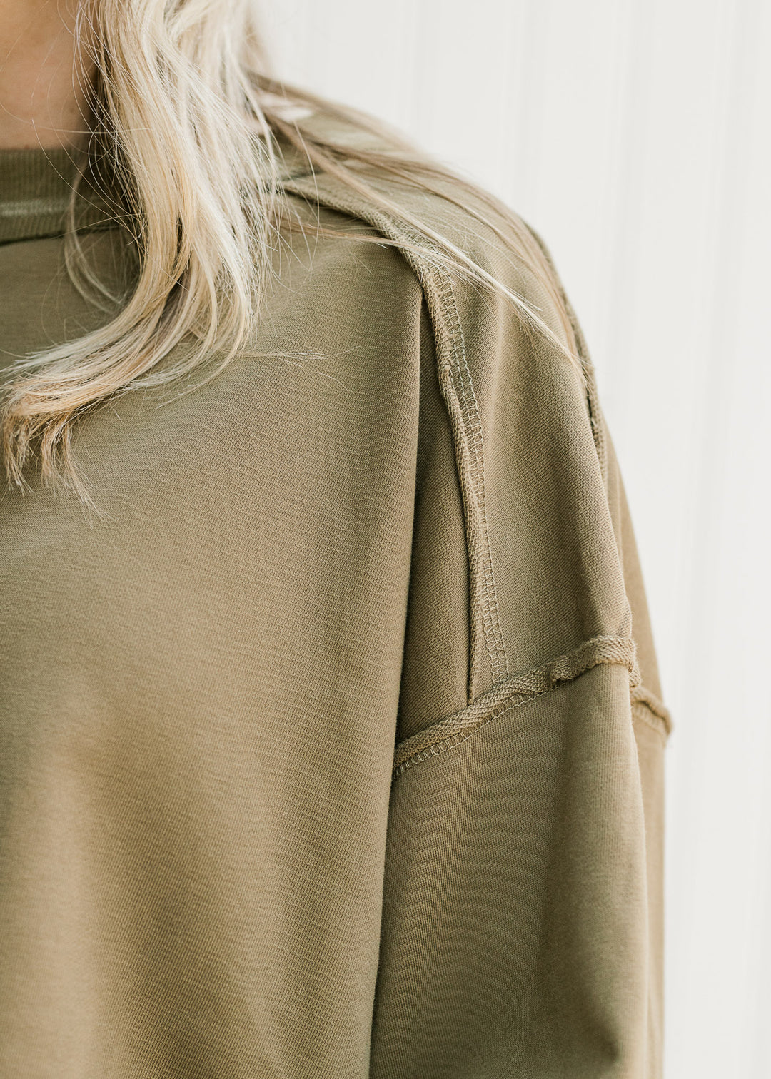 Close up of exposed hem and extended shoulder on an olive lightweight top with a round neck. 