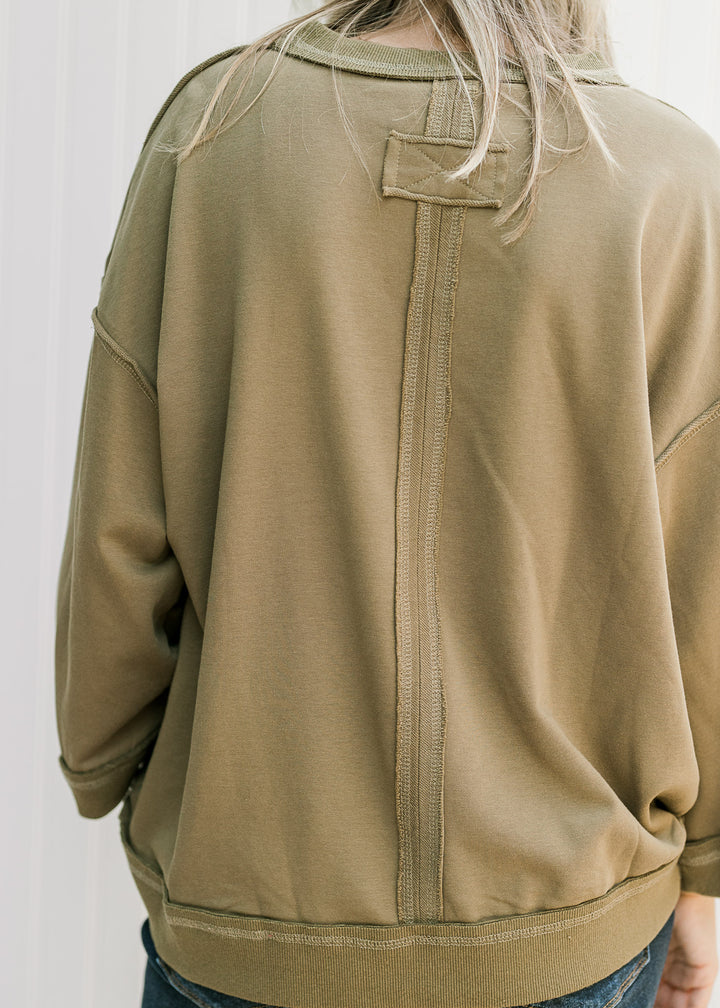 Back view of seam with patch detail, exposed hem and 3/4 sleeves on an olive top. 
