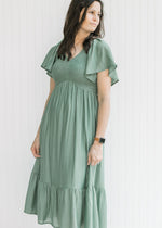 Model wearing a green midi dress with a smocked bodice, short sleeves and ruffle on the hem. 