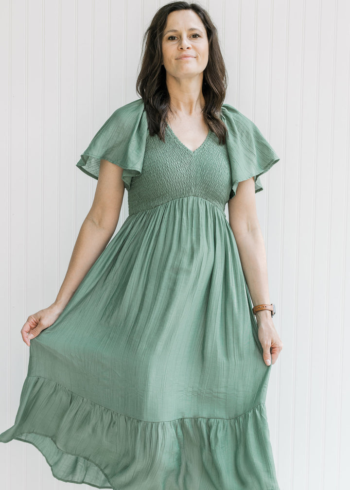 Model holding the skirt on a green midi dress with a smocked bodice and flutter short sleeves.