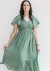 Model holding the skirt on a green midi dress with a smocked bodice and flutter short sleeves.