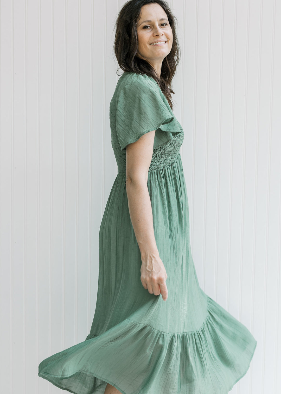 Model wearing a green v-neck midi dress with a smocked bodice and flutter short sleeves. 
