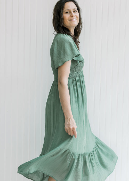 Model wearing a green v-neck midi dress with a smocked bodice and flutter short sleeves. 
