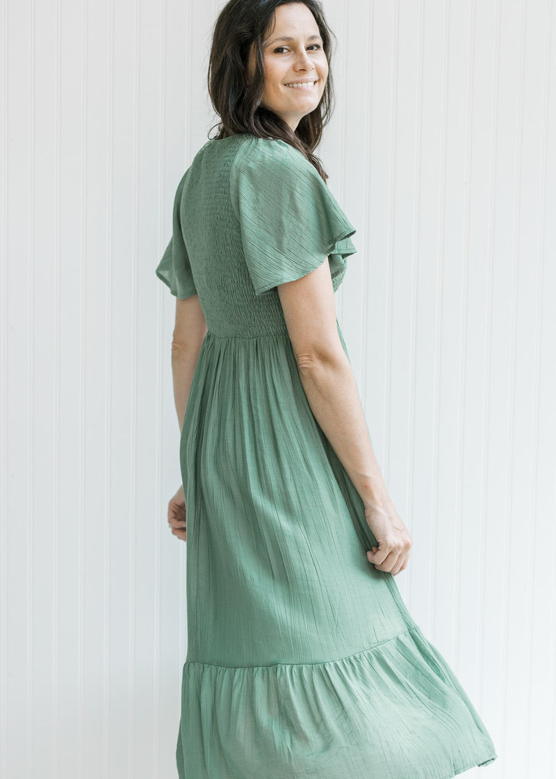Model twirling in a green v-neck midi dress with a smocked bodice and flutter short sleeves.