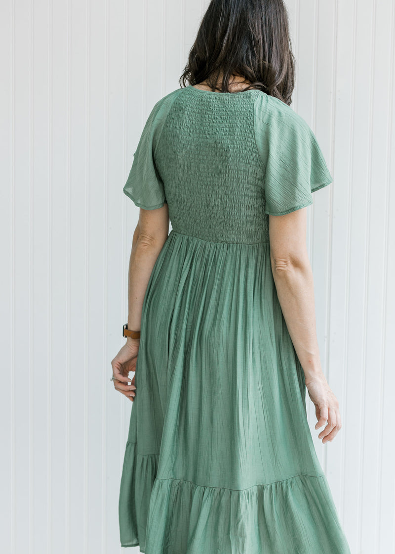 Back view of Model wearing a green midi dress with a smocked bodice and flutter short sleeves.