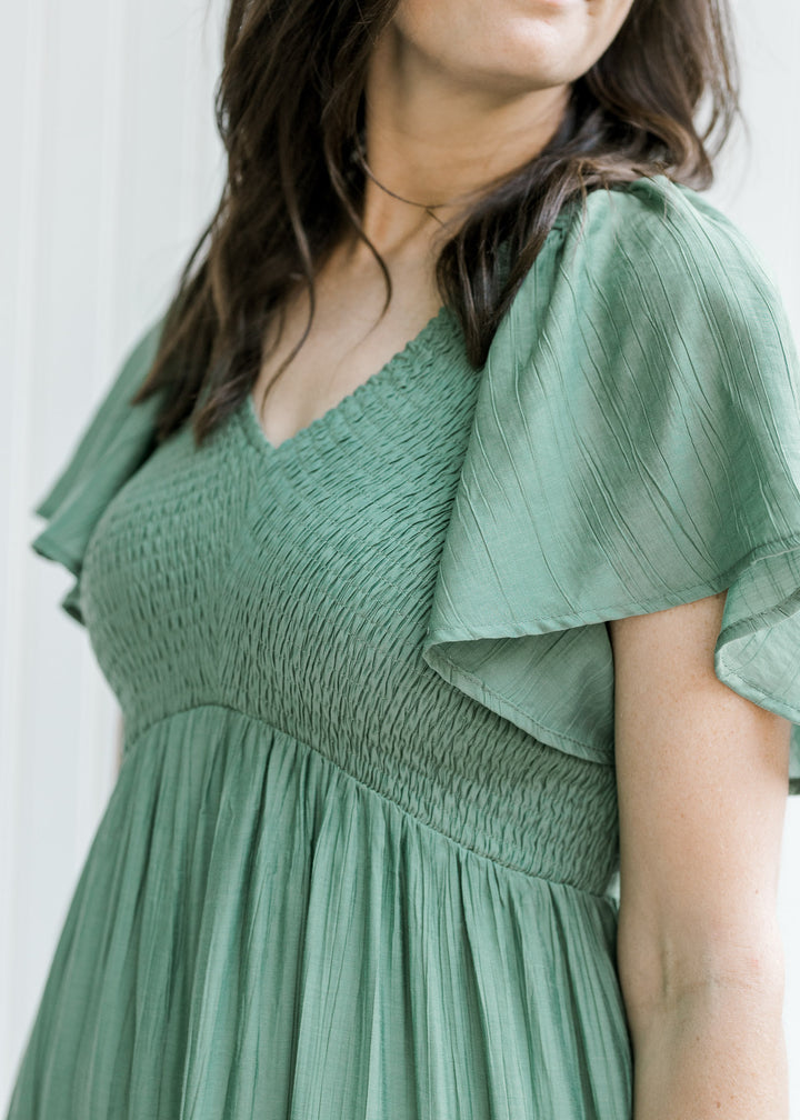 Close up of smocked bodice and flutter short sleeves on a model in a green midi dress. 