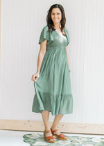 Model wearing heels with a green v-neck midi dress with a smocked bodice and flutter short sleeves.