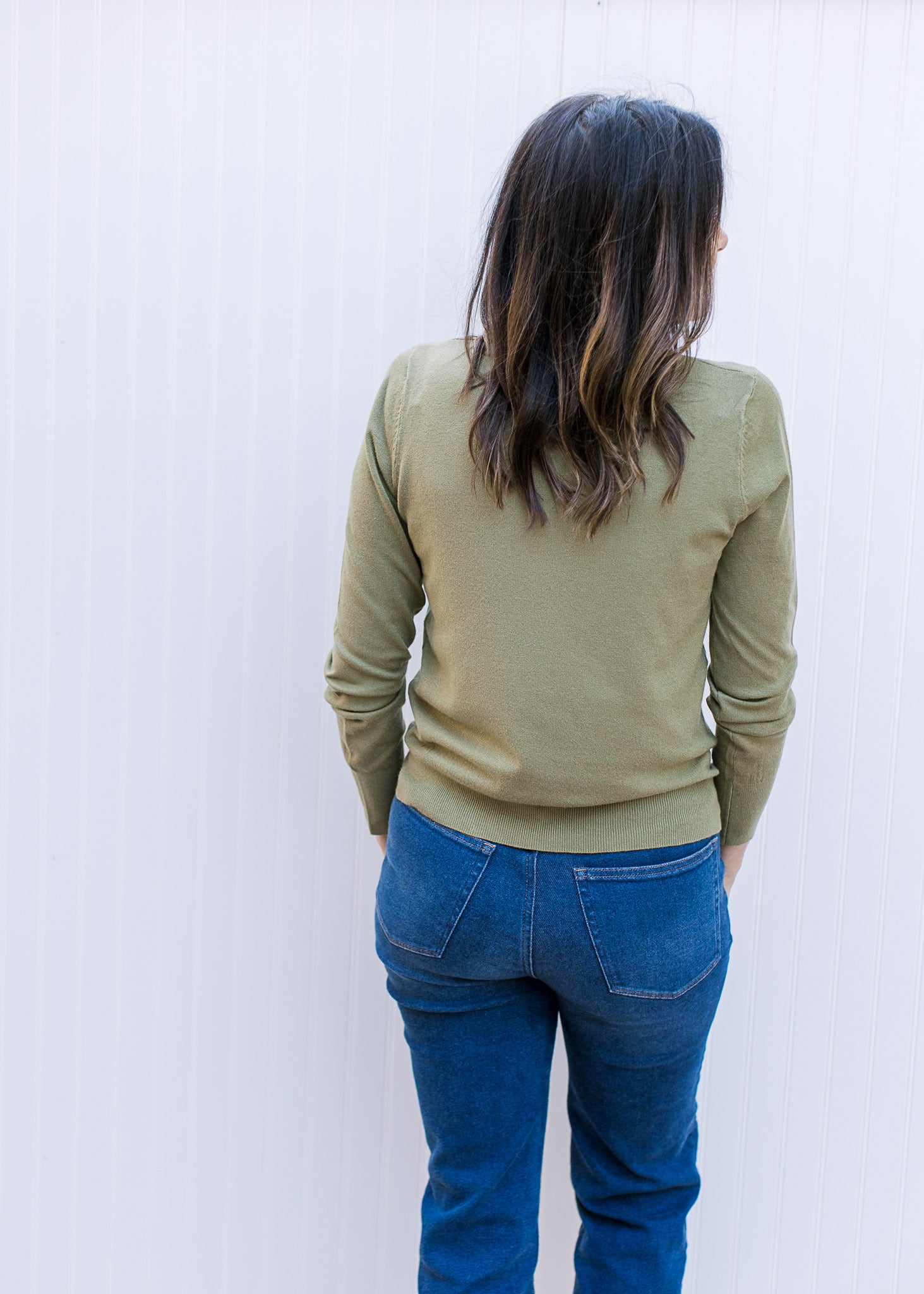 Back view of Model wearing a lightweight olive green sweater with long sleeves and a mock neck. 