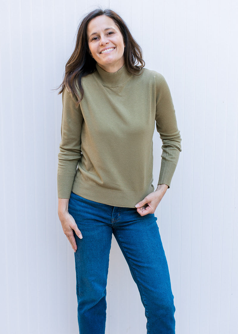 Model wearing a lightweight olive green sweater with long sleeves and a mock neck. 