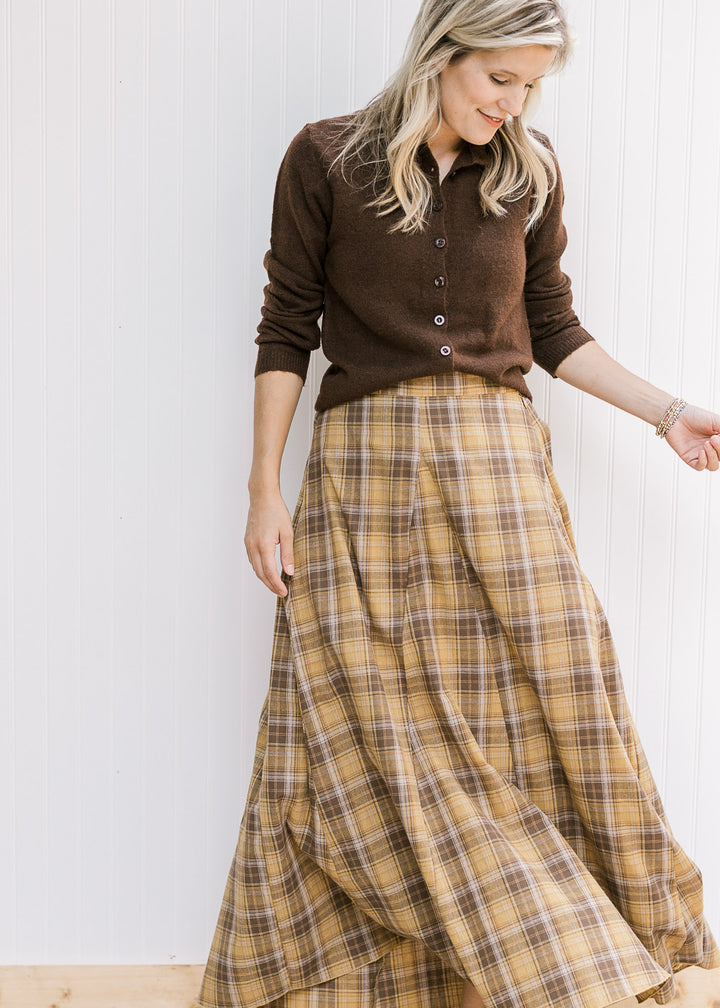 Model wearing brown button up with a flowy gold and brown plaid midi with gored side panels. 