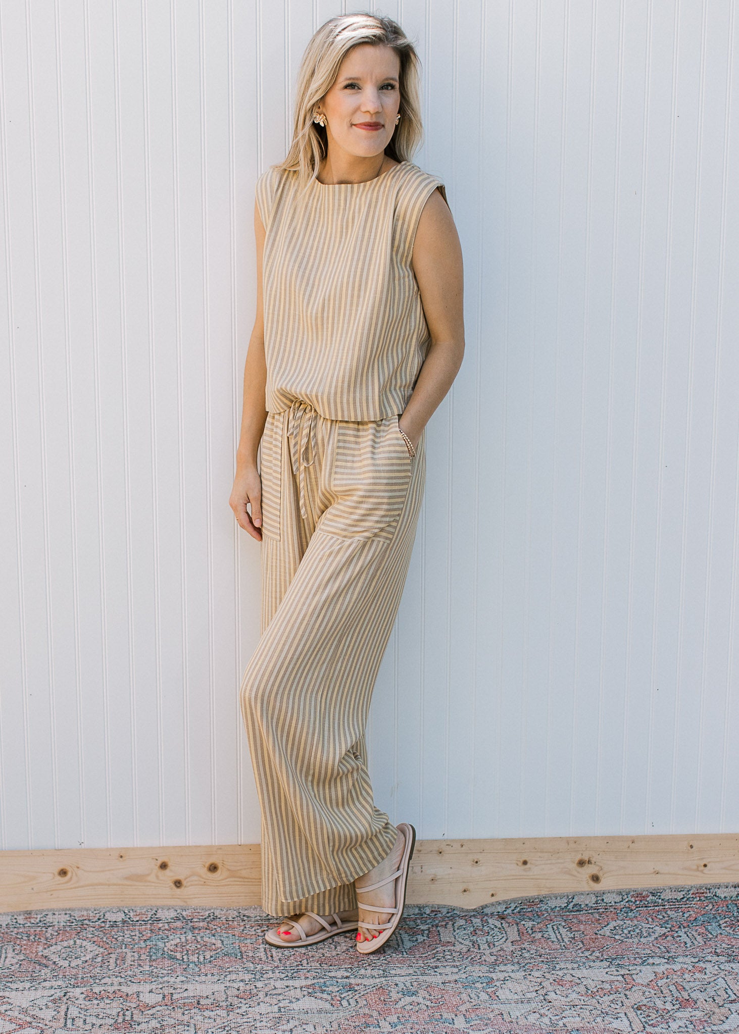 Model wearing a cream and yellow striped pants set with a sleeveless top and wide leg bottoms. 